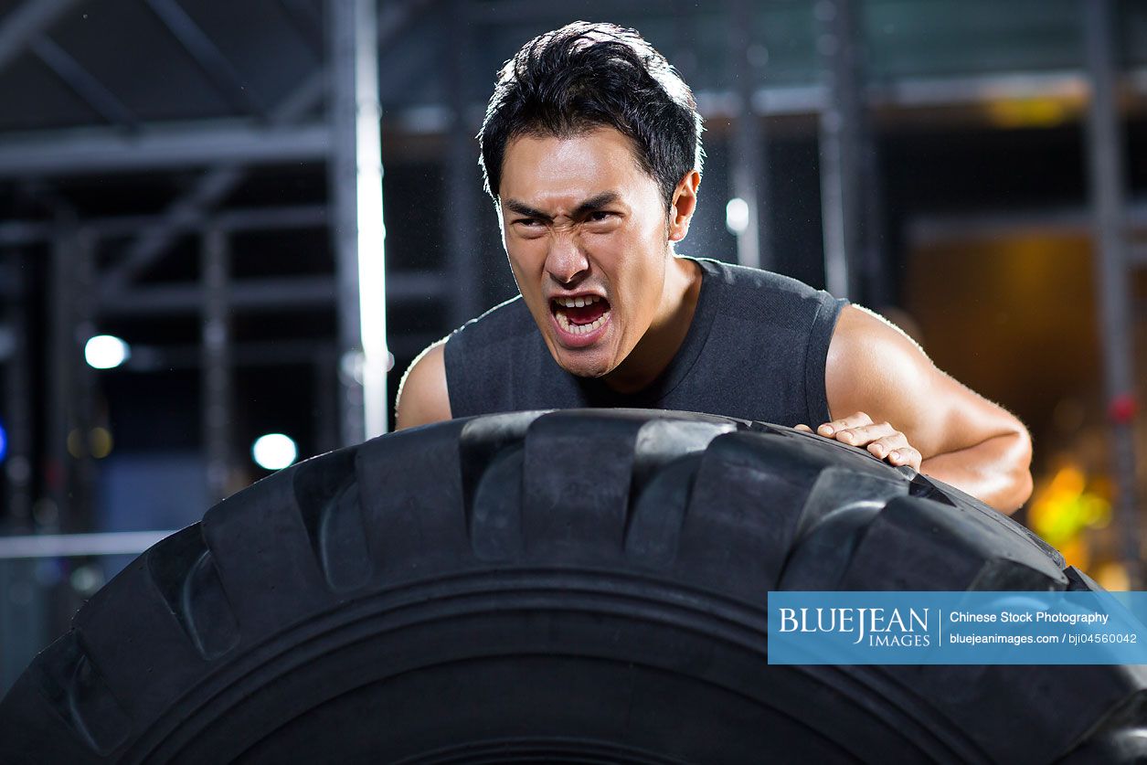 Young Chinese man pushing large tire in crossfit gym