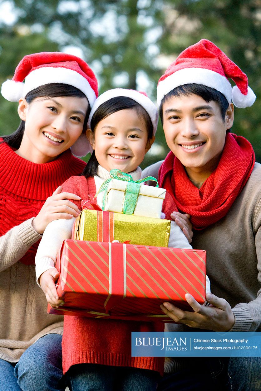 Chinese multi generation family holding Christmas gifts in santa hats