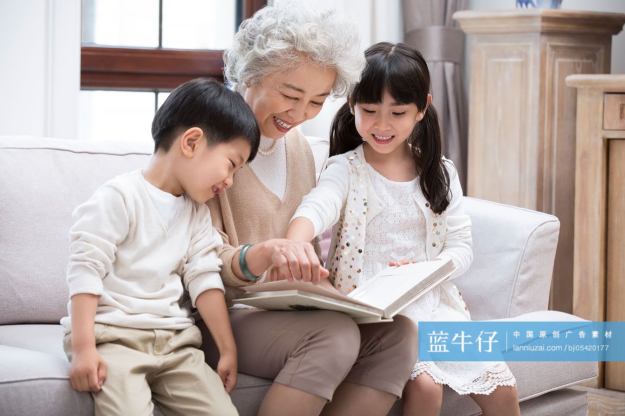 开心的奶奶和孙子孙女在沙发上看相册