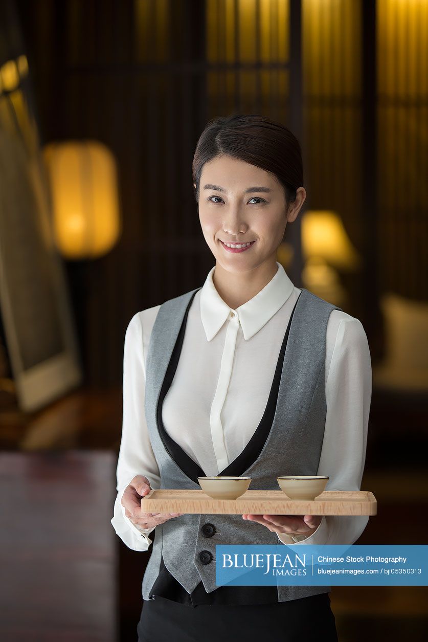 Elegant Chinese waitress holding two cups of tea