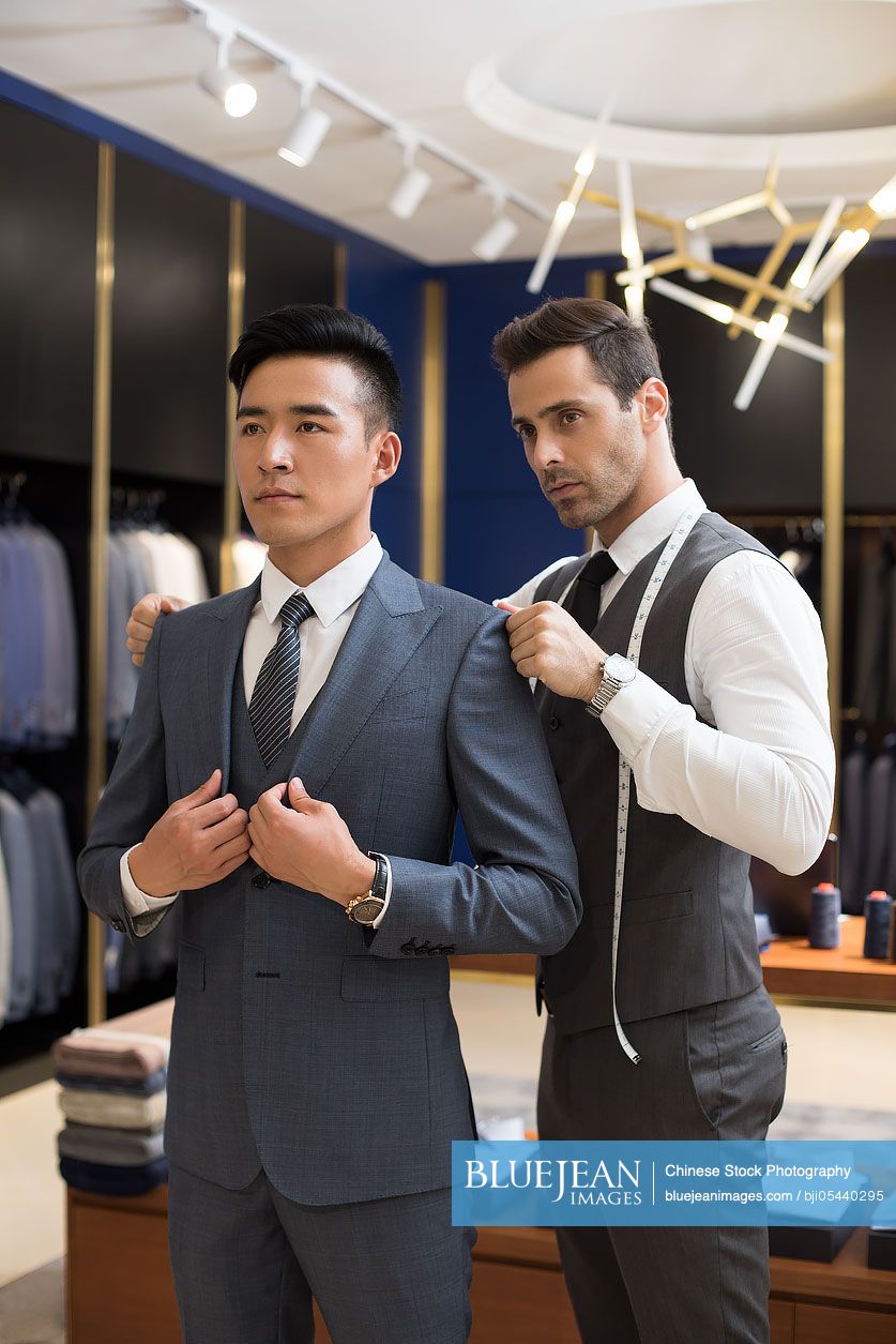 Chinese fashion designer examining suit on customer