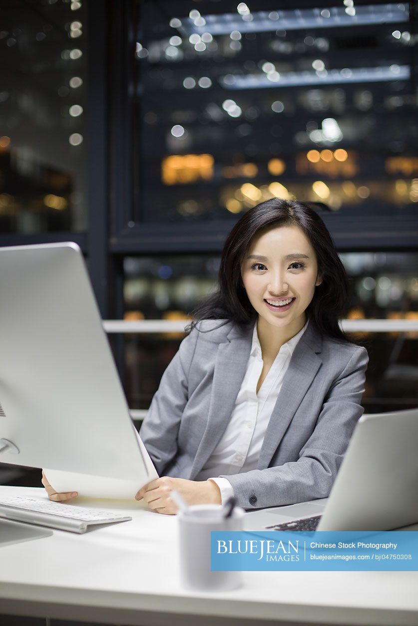 Happy Chinese businesswoman working late in office