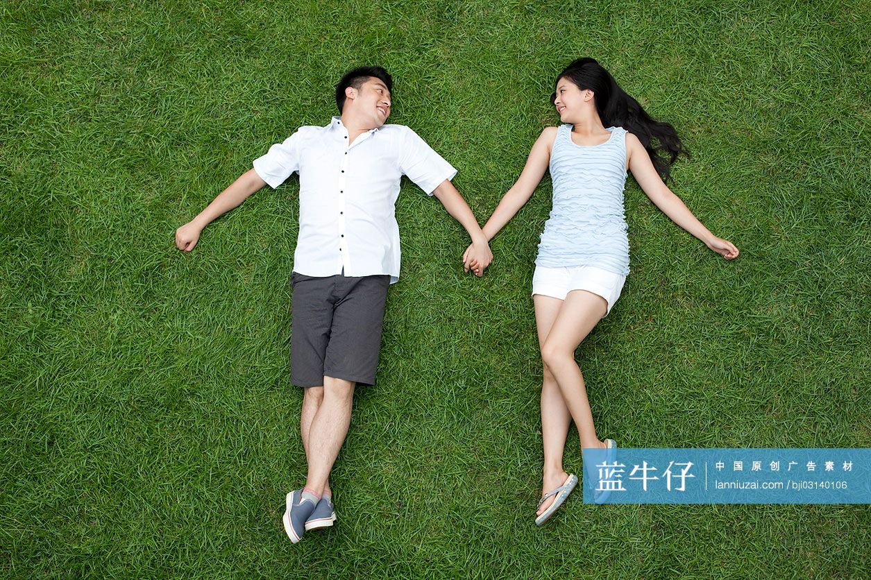 年轻情侣手牵手躺在草地上