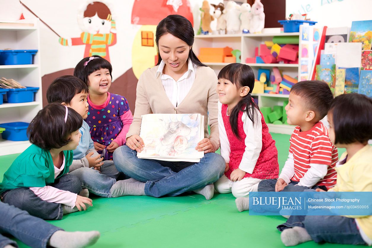 Female Chinese teacher showing kindergarten children picture book