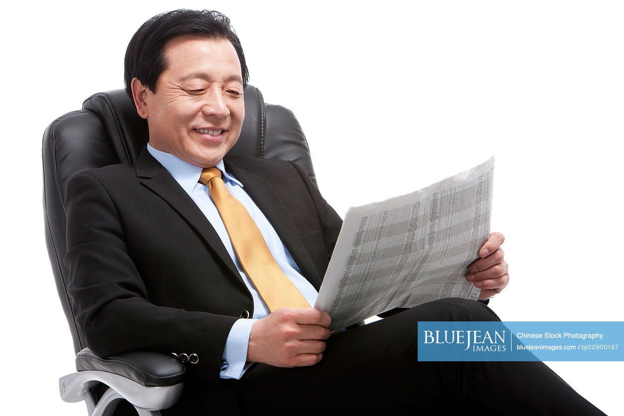 Senior Chinese businessman reading newspaper on director's chair