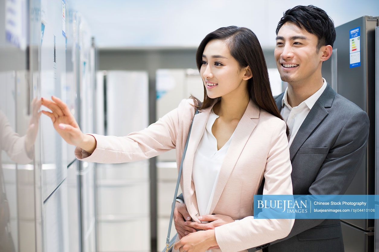 Young Chinese couple buying refrigerator in electronics store