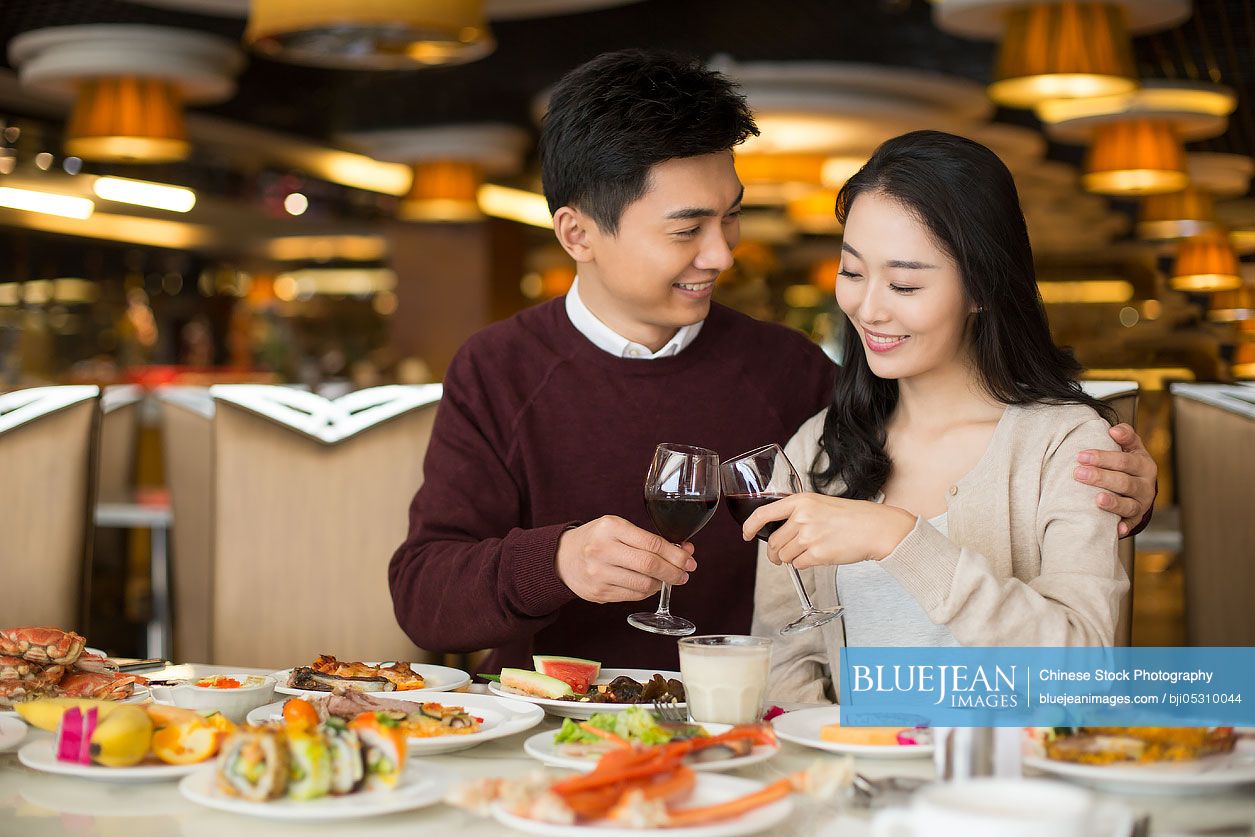 Cheerful young Chinese couple toasting with red wine