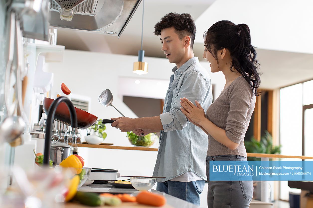 Happy young Chinese couple cooking in kitchen