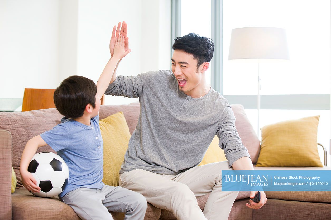 Excited Chinese father and son watching football on TV