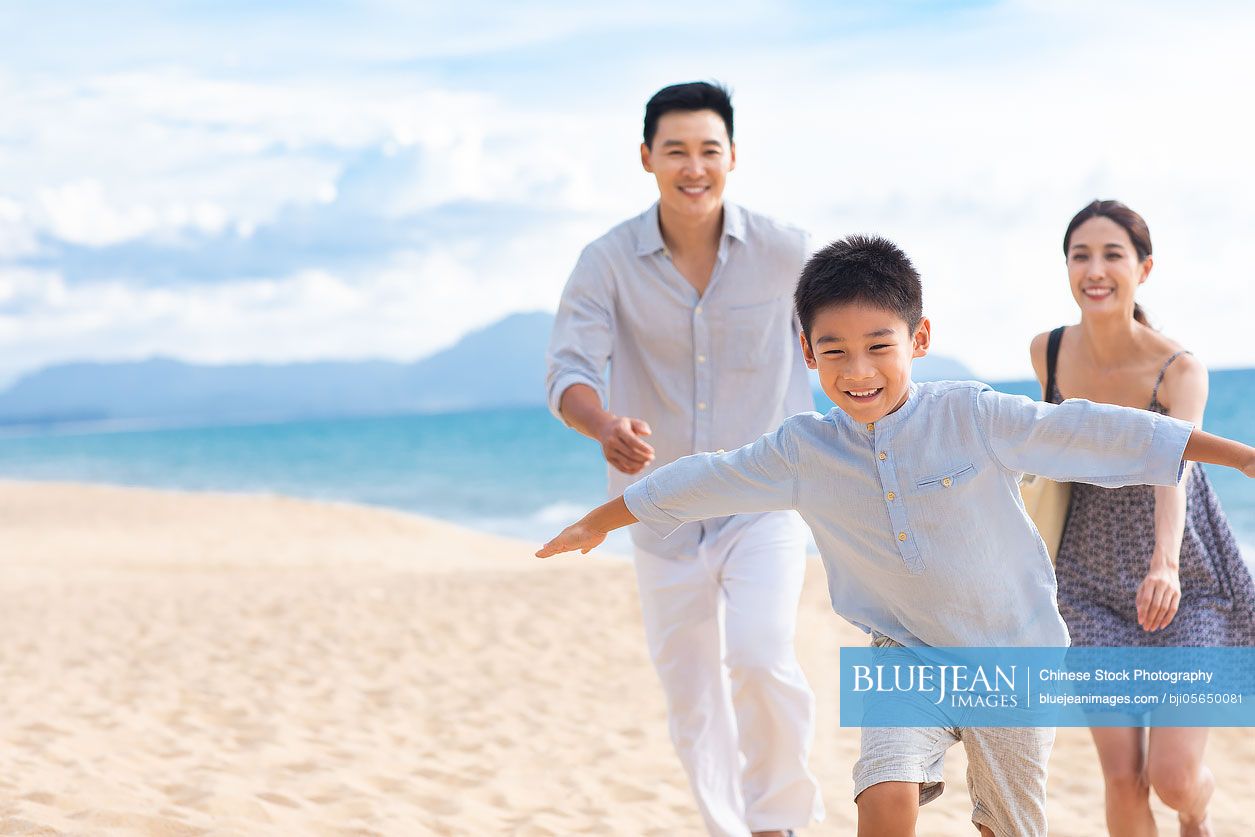 Happy young Chinese family pretending to be flying on beach