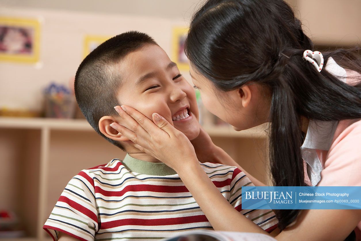 Chinese Teacher And Young Child Reading A Book, Smiling At Each Other