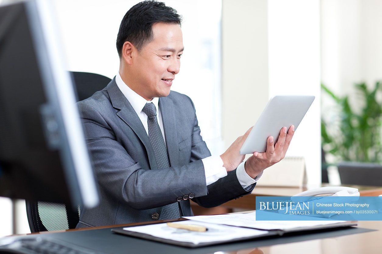 Mature Chinese businessman using digital tablet in office