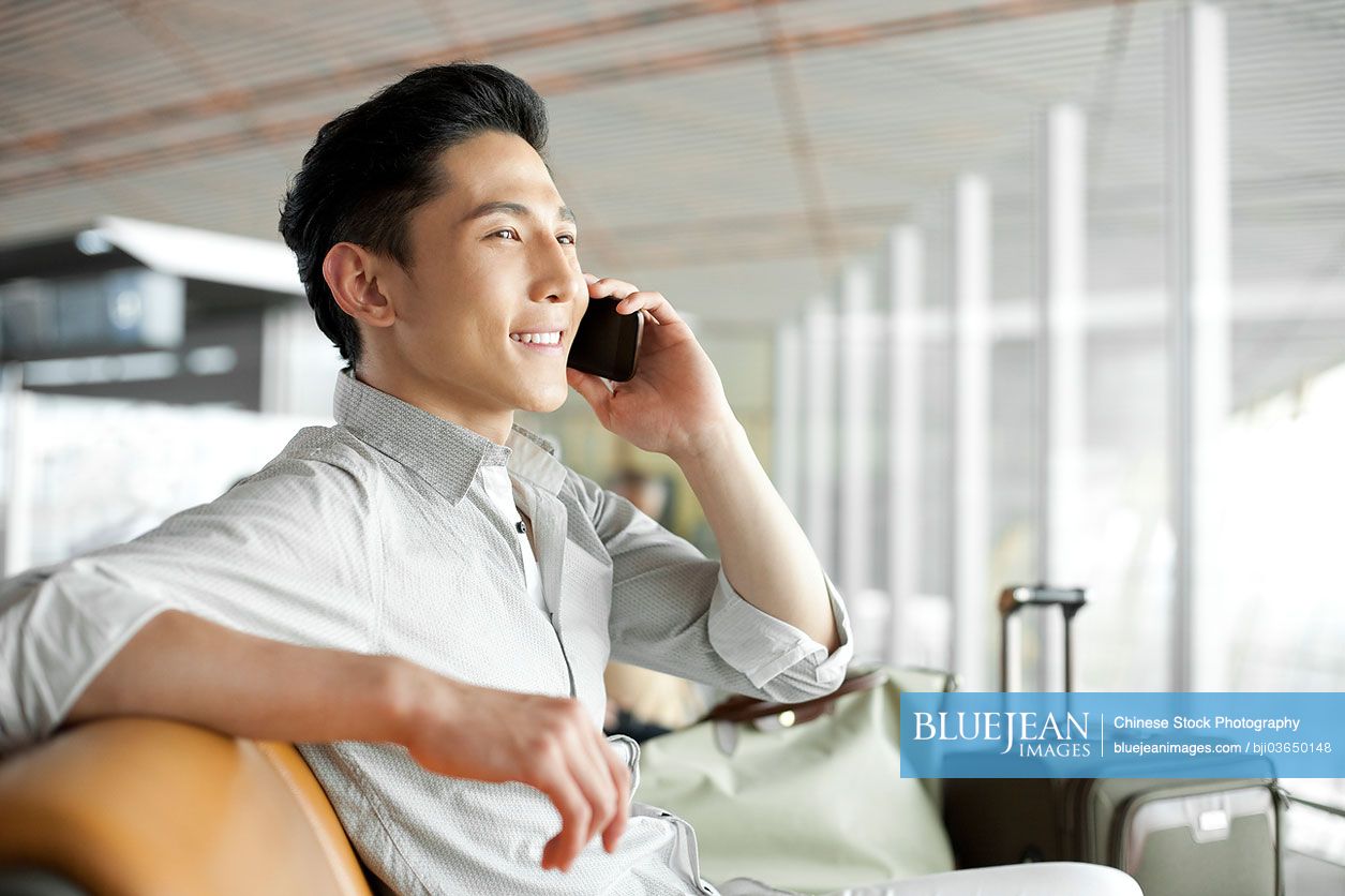 Young Chinese man talking on the phone in airport lounge