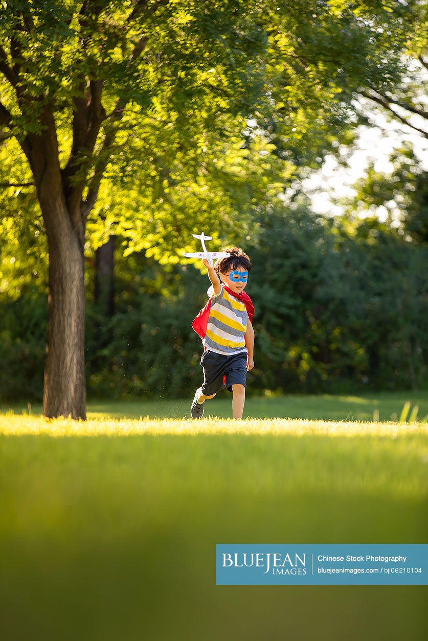 Little Chinese boy in superman costume playing on meadow