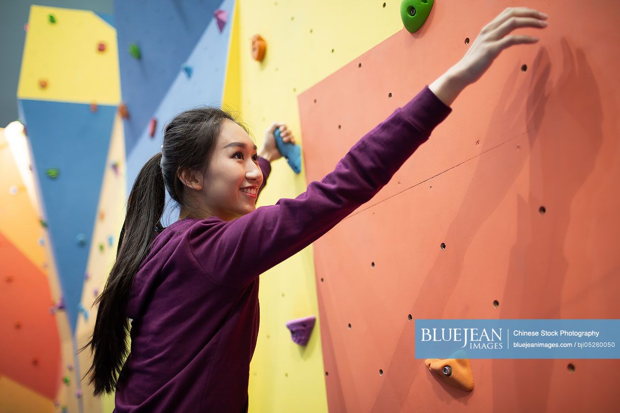 Happy young Chinese woman climbing a climbing wall at gym