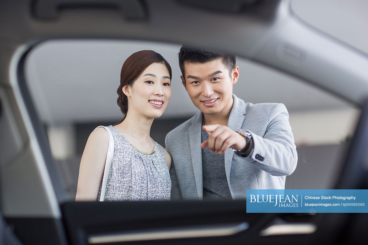 Young Chinese couple looking at new car in showroom