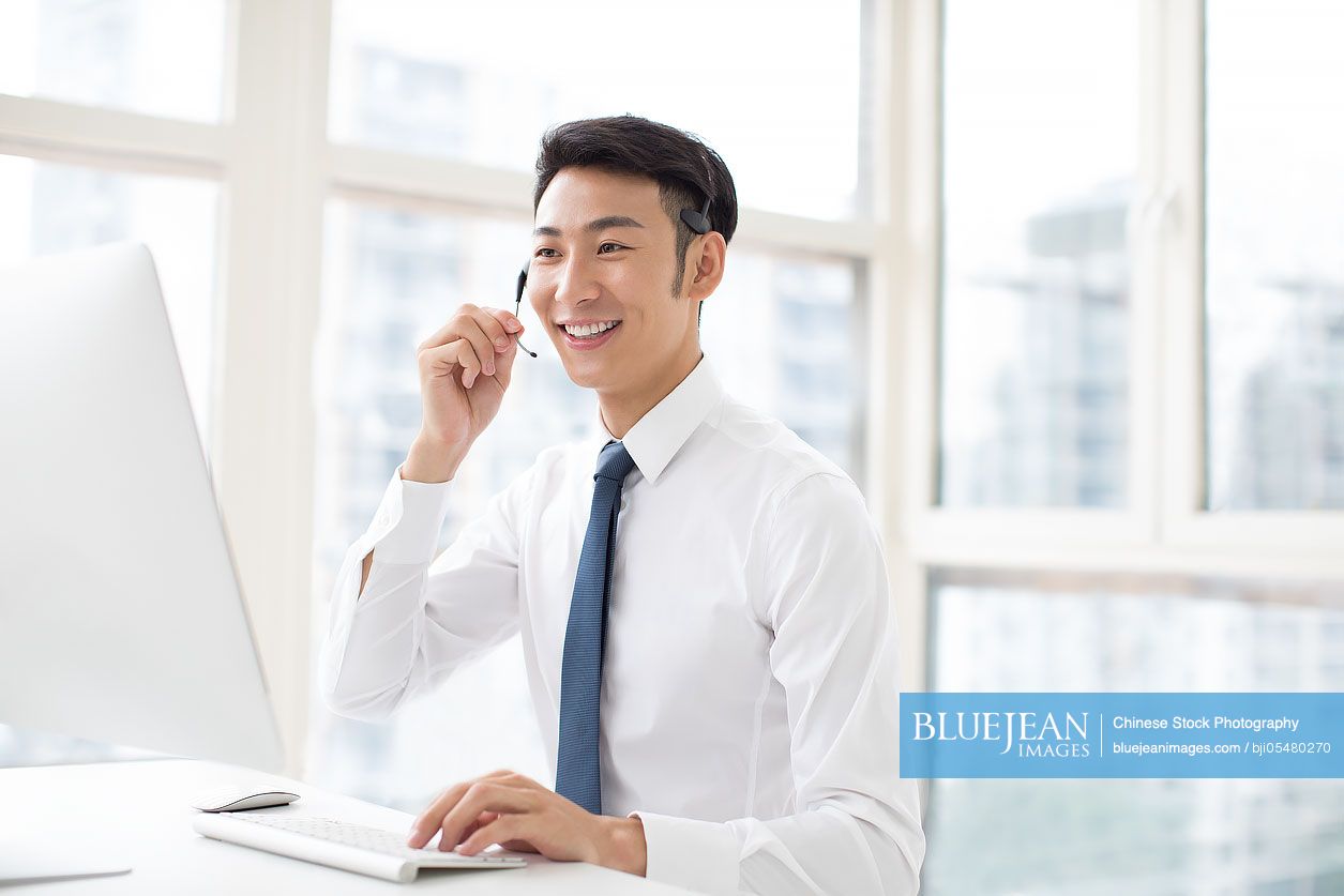 Cheerful young Chinese businessman working in office with headset