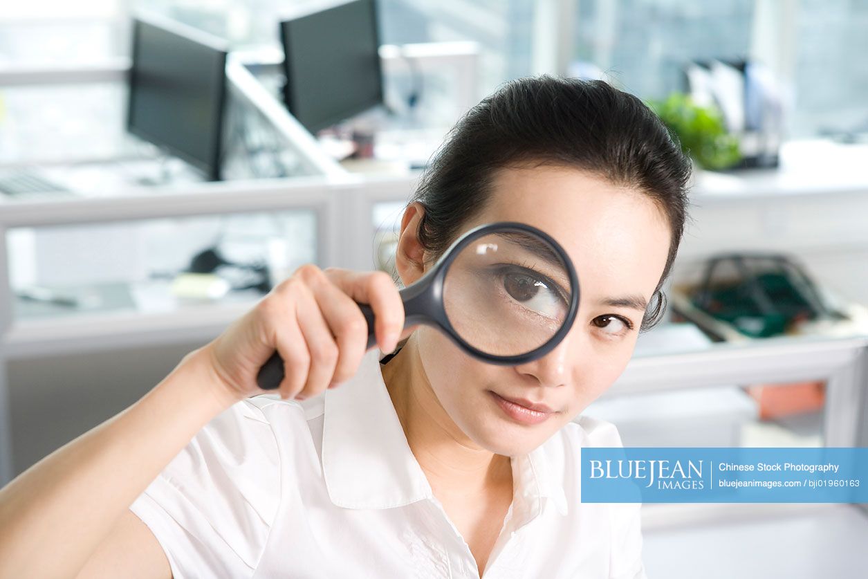 Chinese office worker examining through a magnifying glass