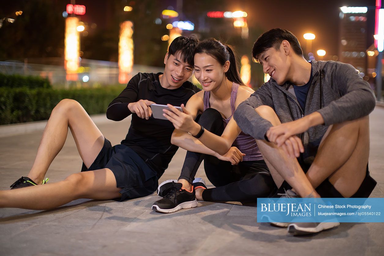 Young Chinese friends using smartphone outdoors