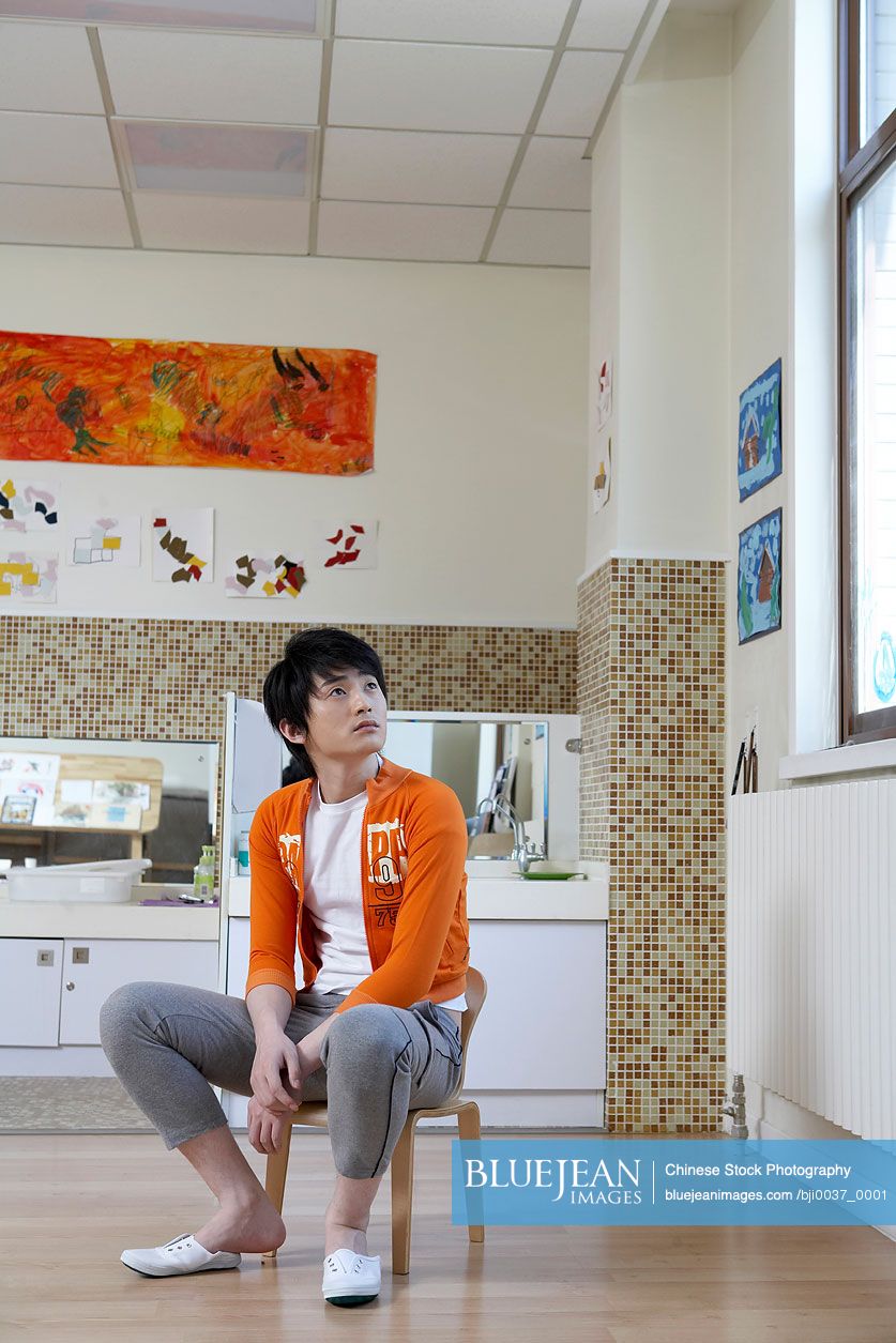 Chinese Young Man Sitting On A Chair, Looking Pensive