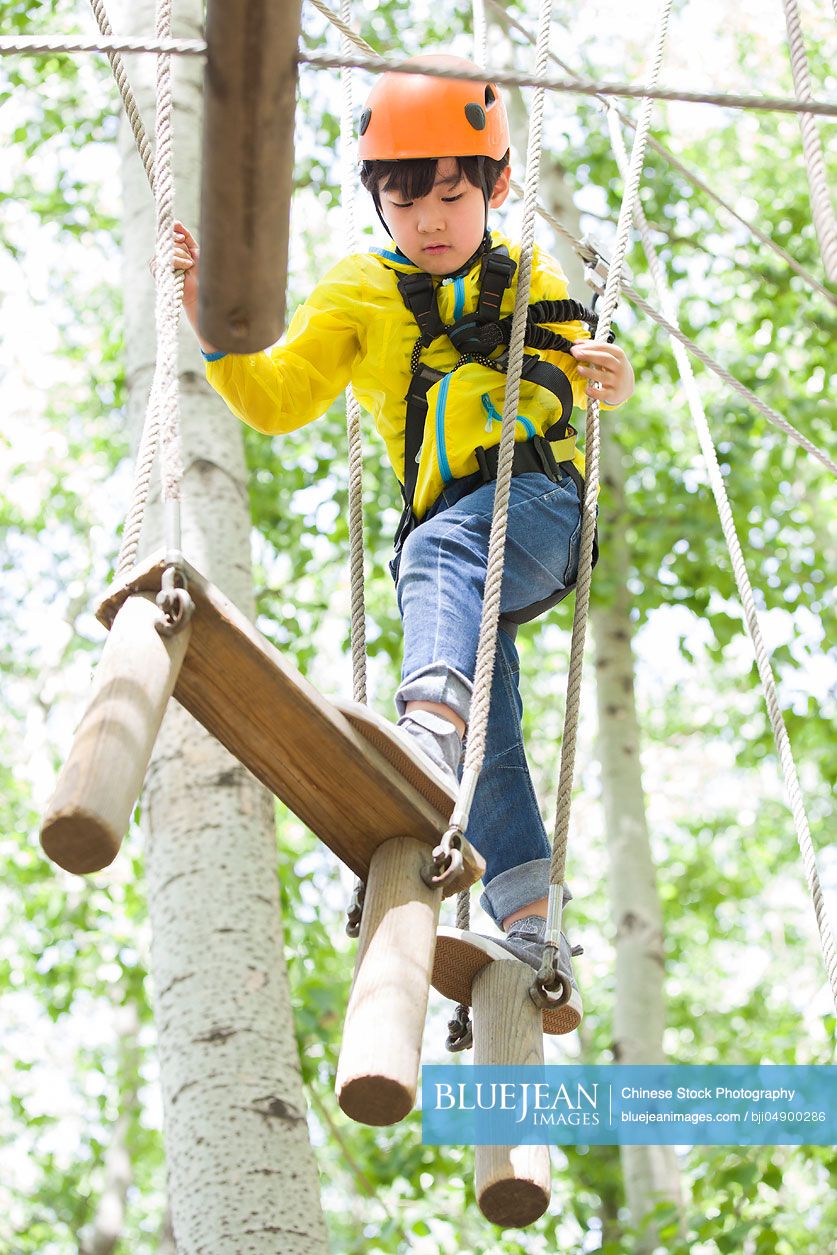 Little Chinese boy playing in tree top adventure park