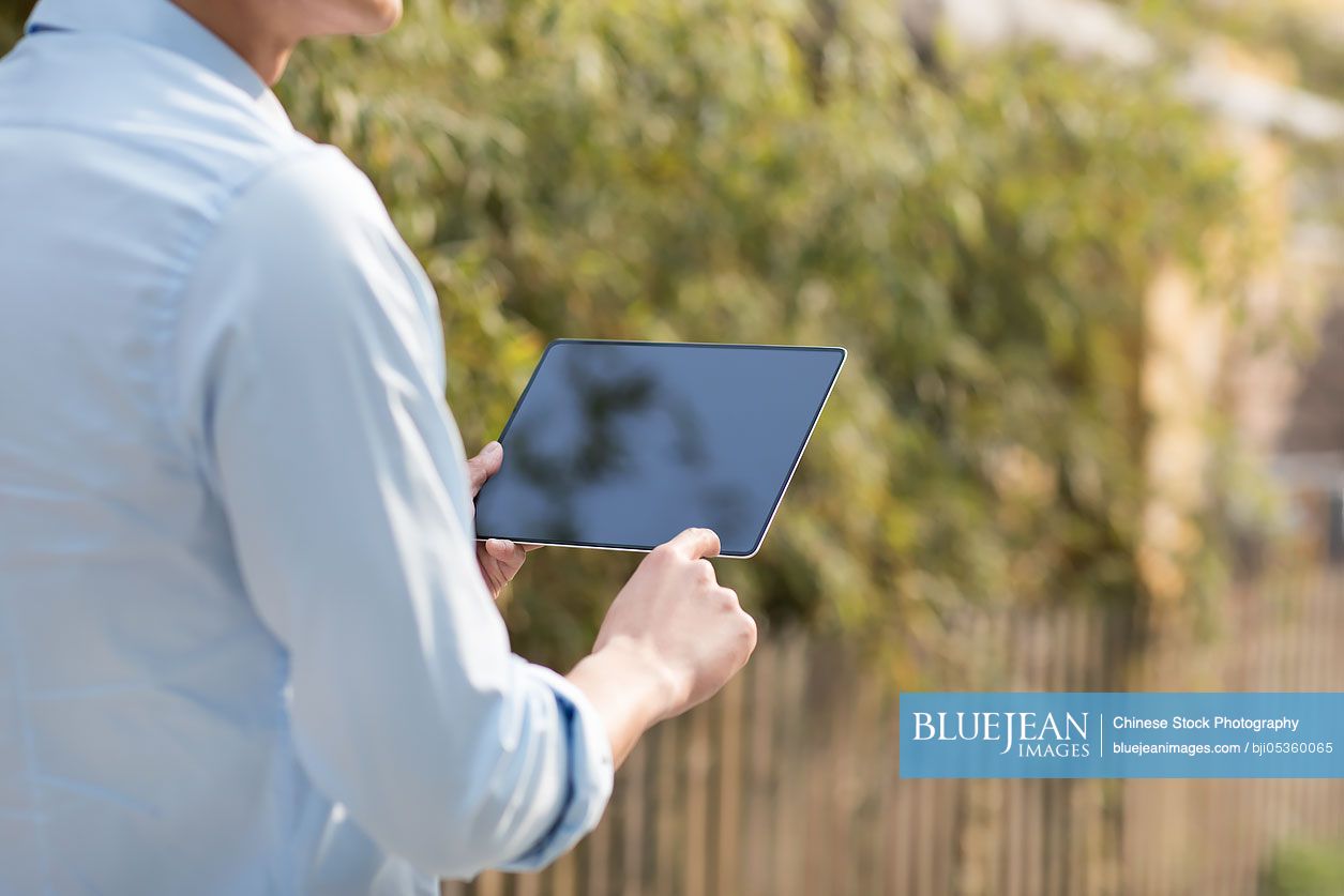 Young Chinese businessman holding a digital tablet outdoors