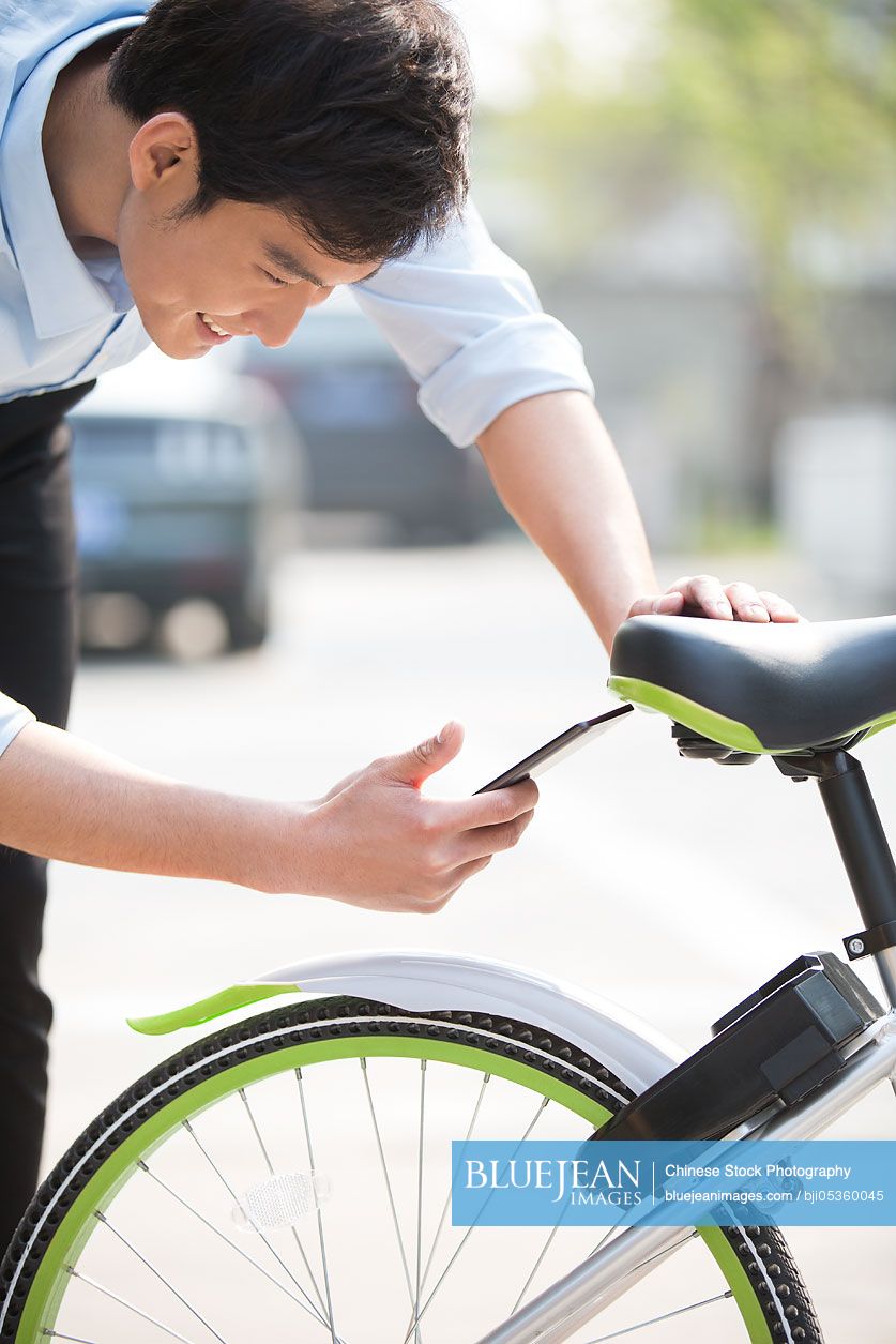 Young Chinese man scanning a QR code to unlock a share bike