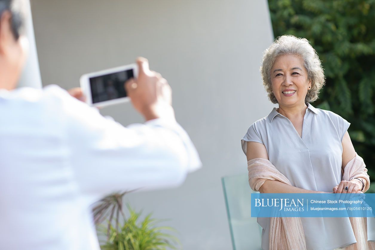 Happy senior Chinese couple using smartphone on balcony