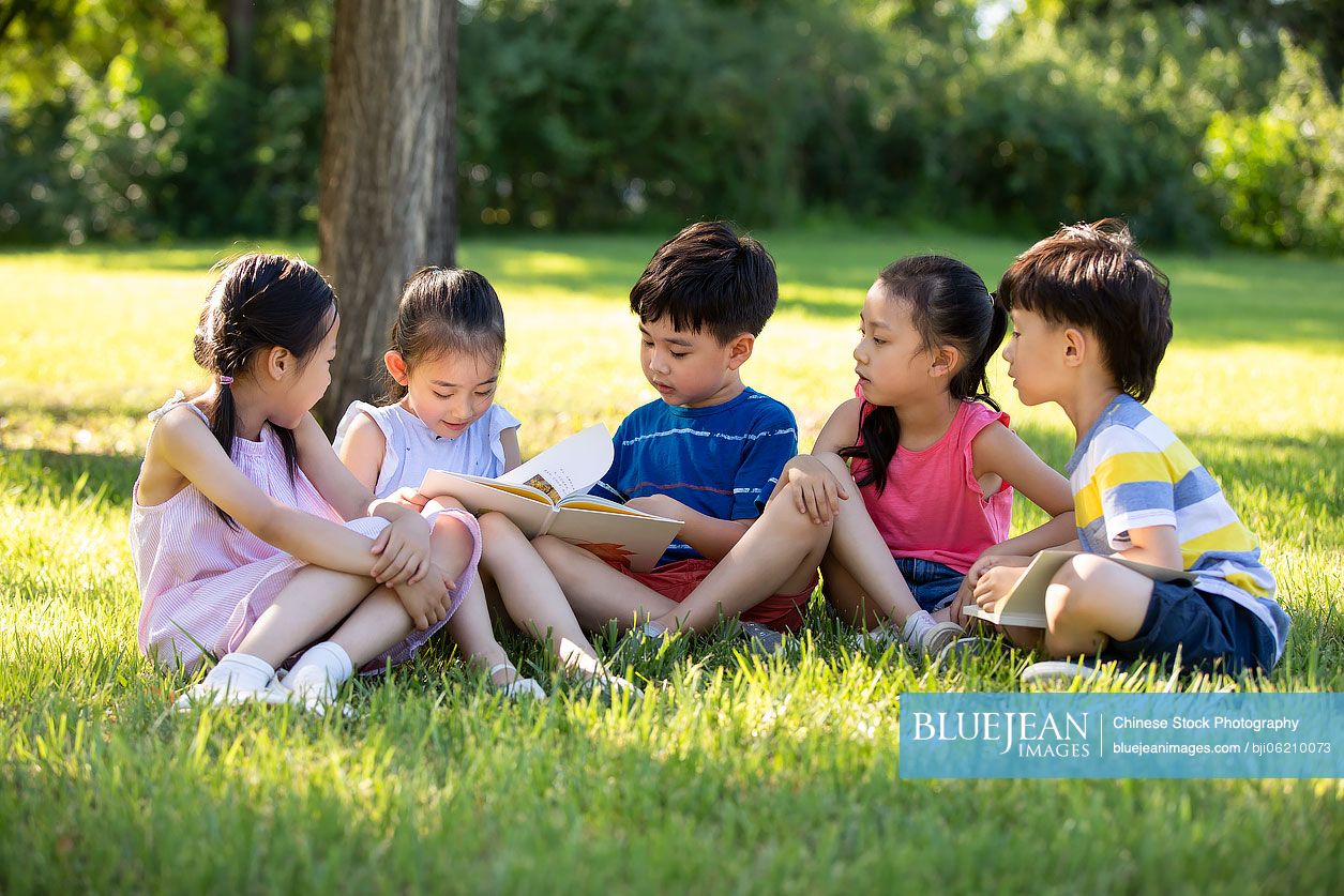 Happy Chinese children reading book on meadow