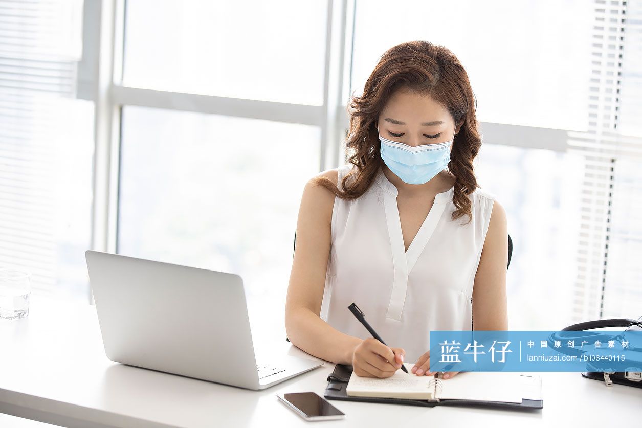 年轻的商务女士戴着口罩工作