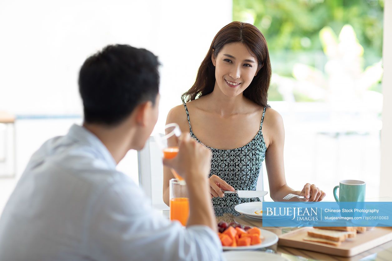 Happy young Chinese couple having breakfast in hotel room