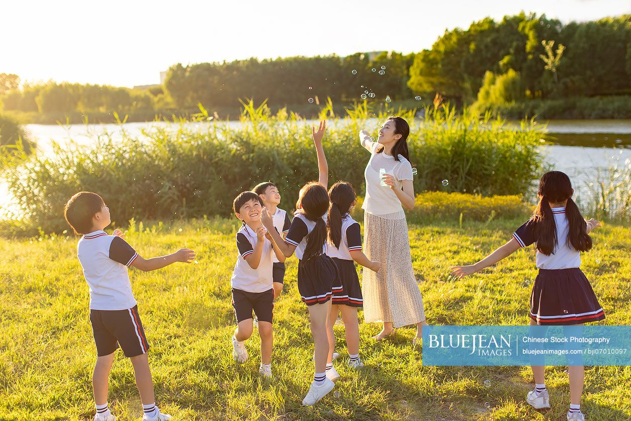 Cheerful Chinese school children and their teacher blowing bubbles on ...