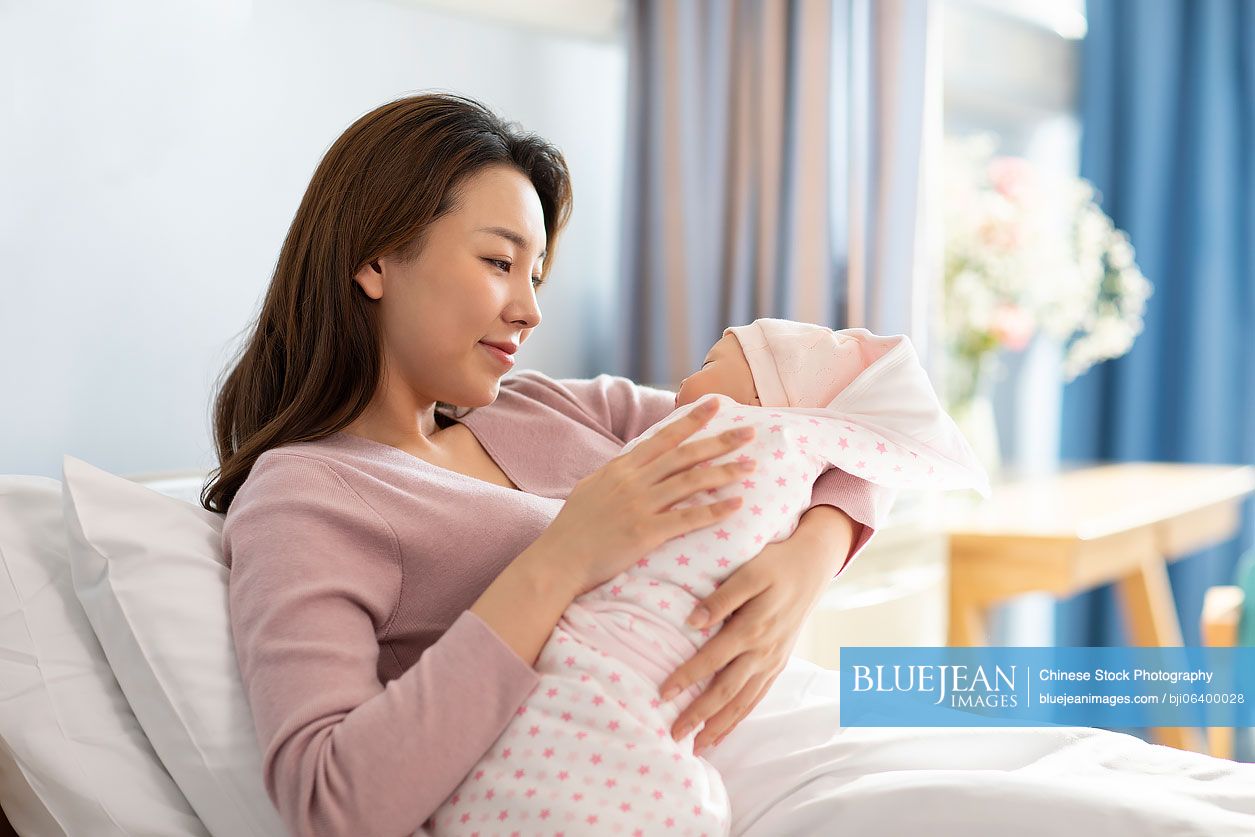 Young Chinese mother holding newborn baby in hospital ward