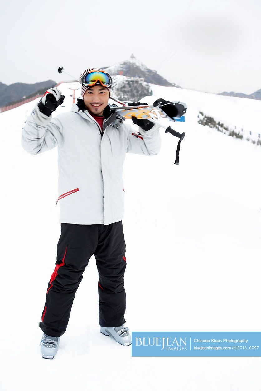 Chinese man standing on ski field, holding skis