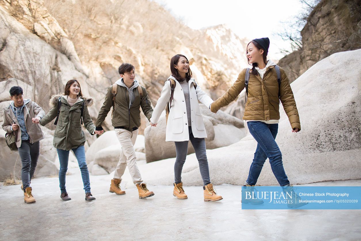 Happy young Chinese friends holding hands enjoying winter outing