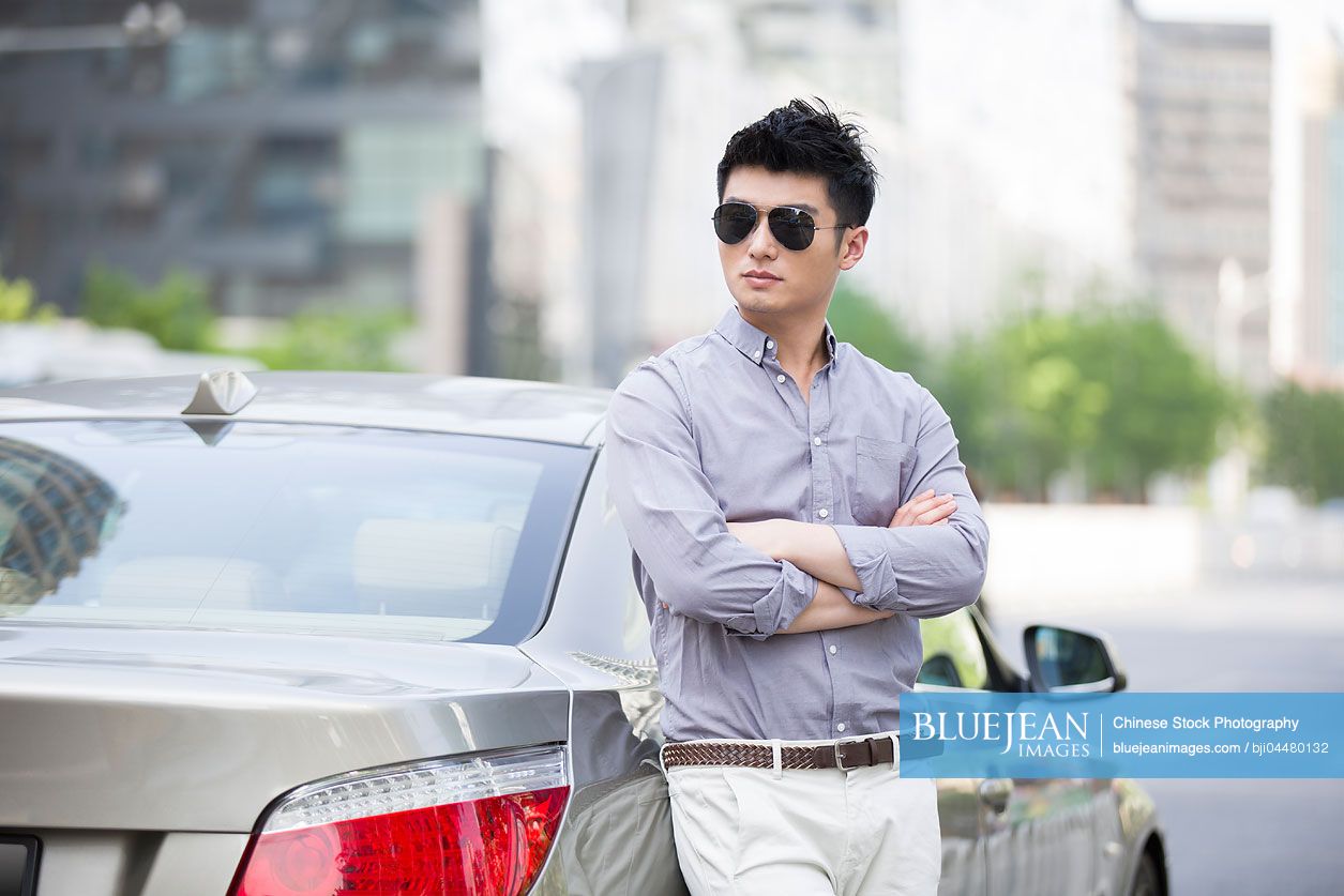Young Chinese man leaning against his car