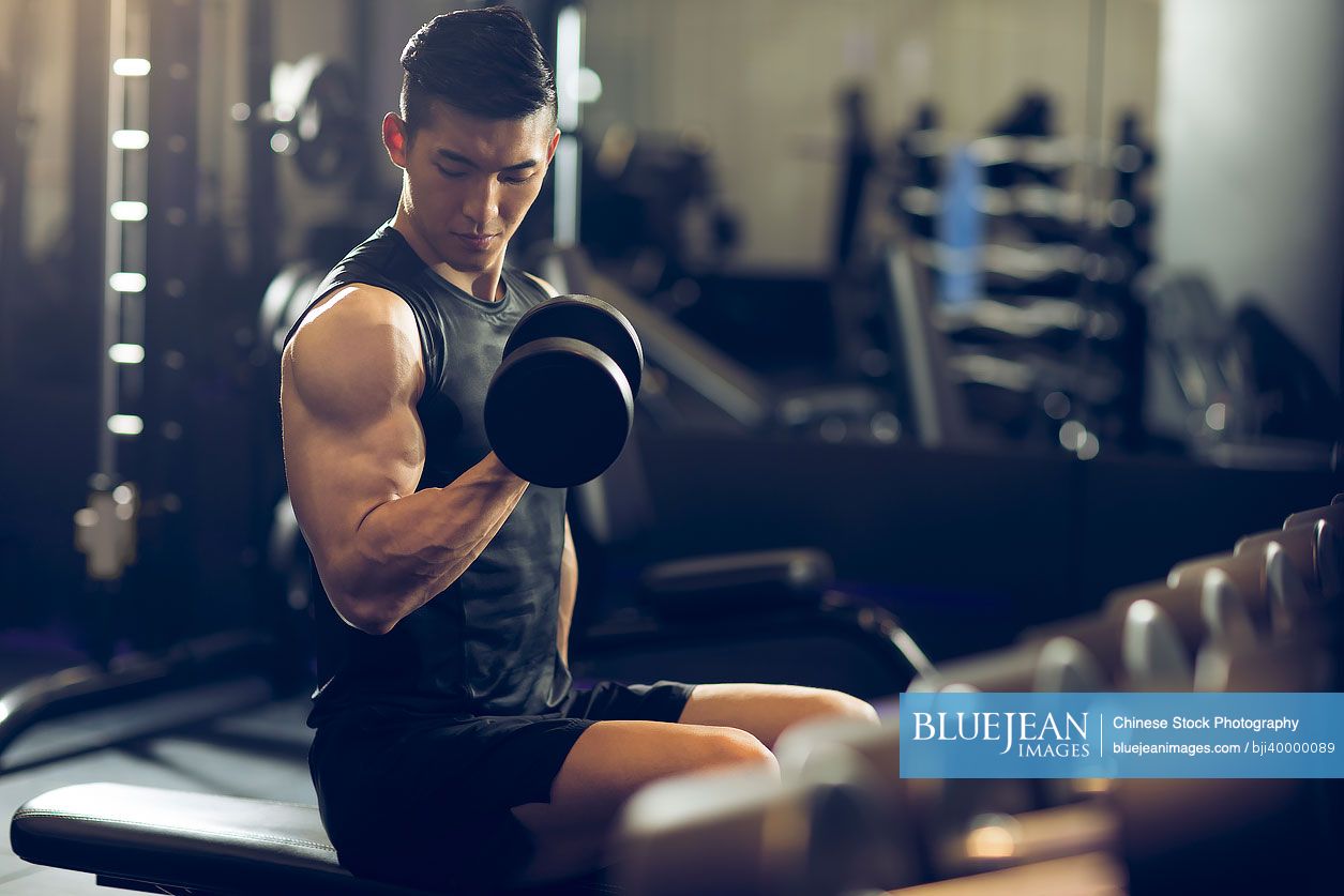 Young Chinese man working out with dumbbell at gym