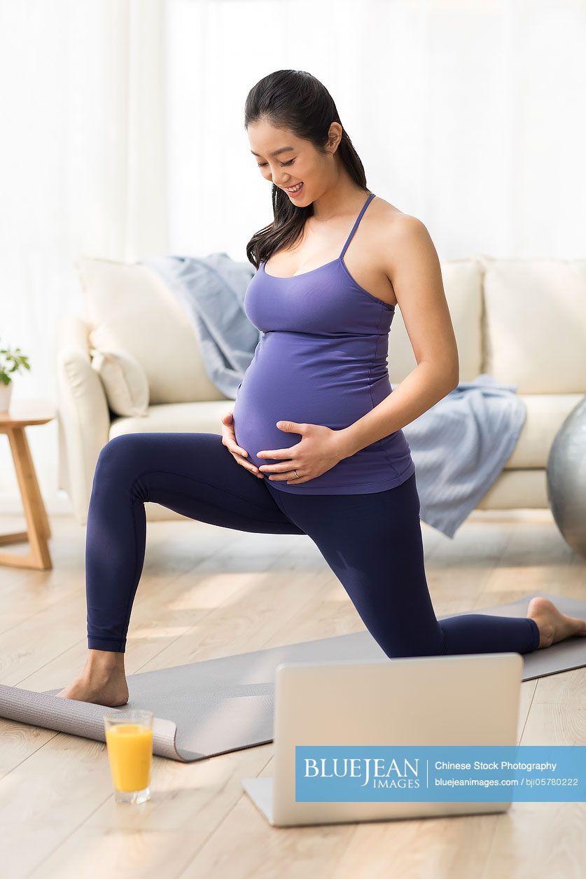 Cheerful Chinese pregnant woman practicing yoga at home