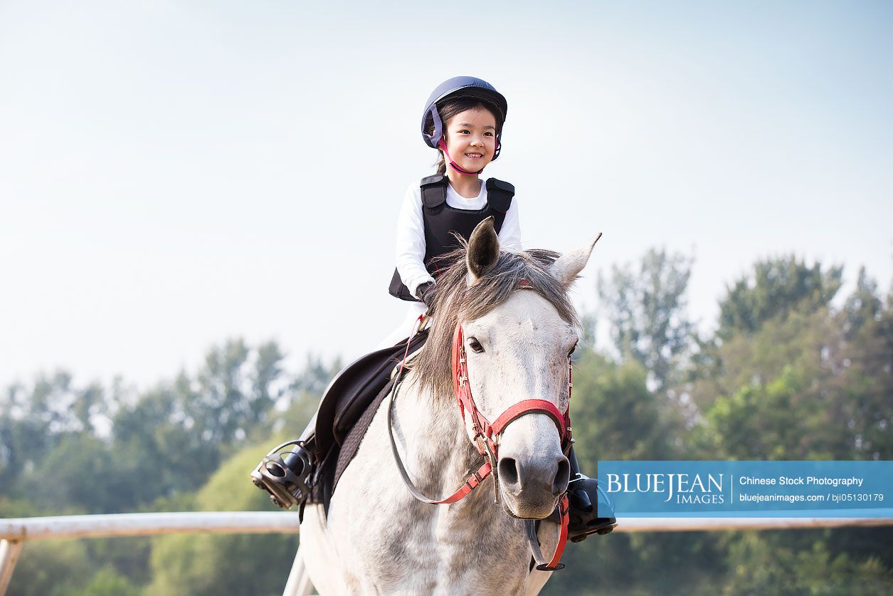 Cheerful little Chinese girl riding horse