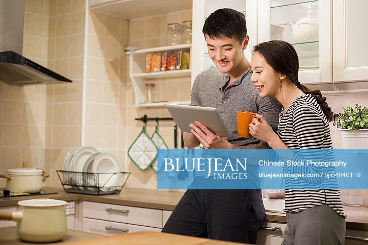 Young Chinese couple using digital tablet in kitchen