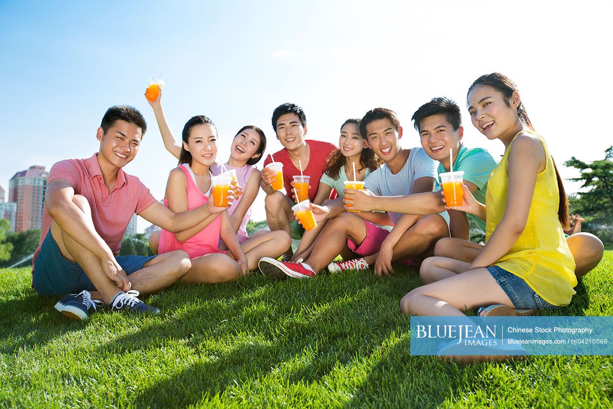 Cheerful young Chinese adults holding juice sitting on grass