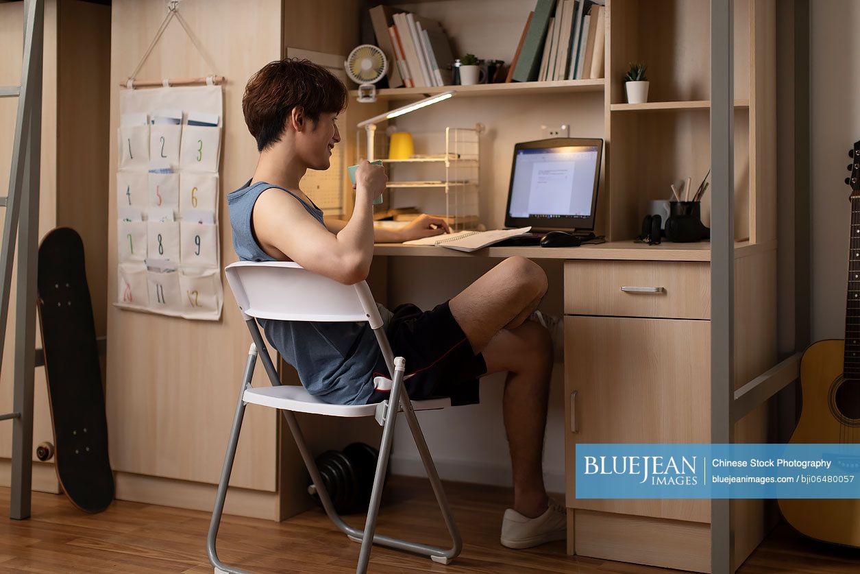 Young Chinese university student using laptop in dormitory