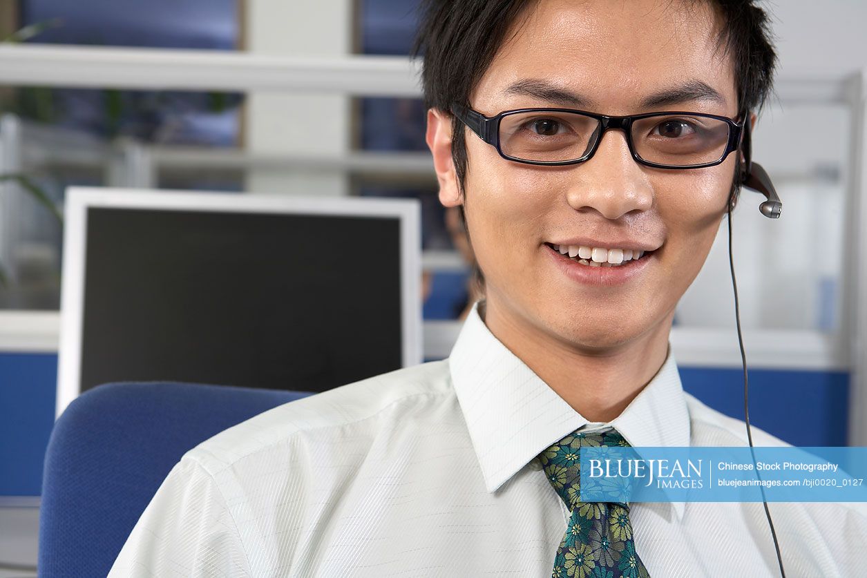 Chinese man in call center wearing a headset and smiling