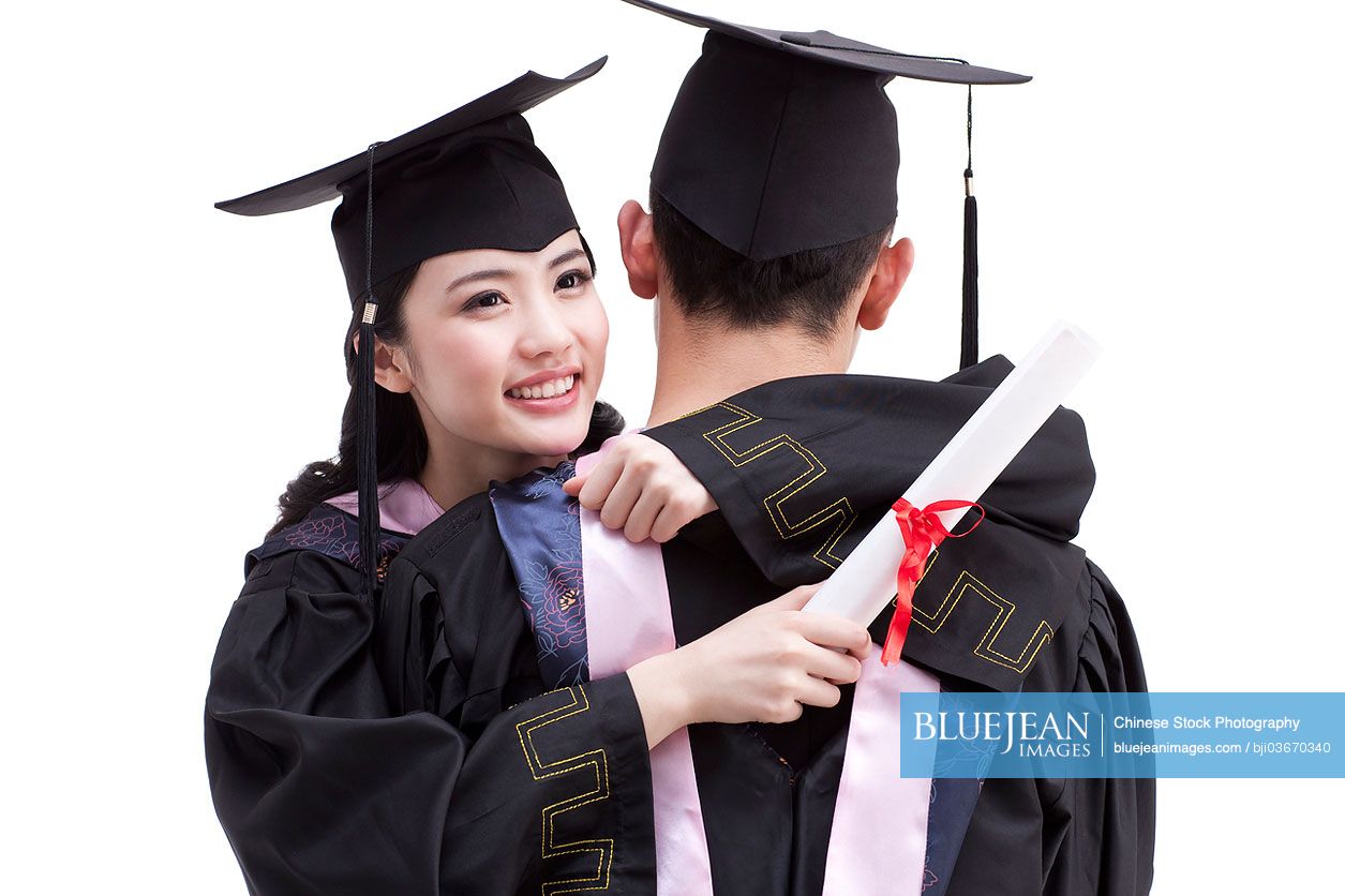 Happy Chinese college graduates in graduation gowns embracing