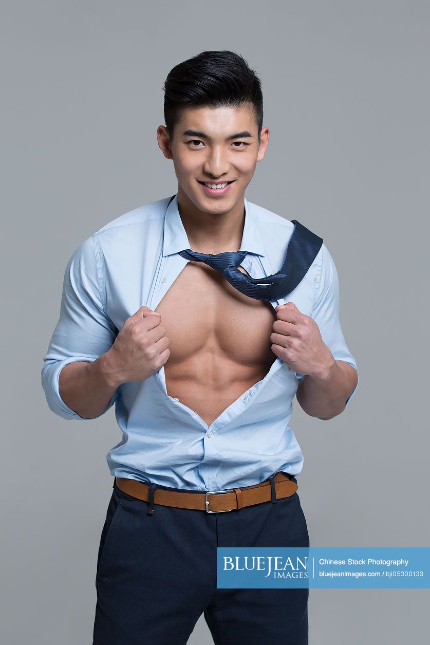 Cheerful young Chinese businessman showing muscles