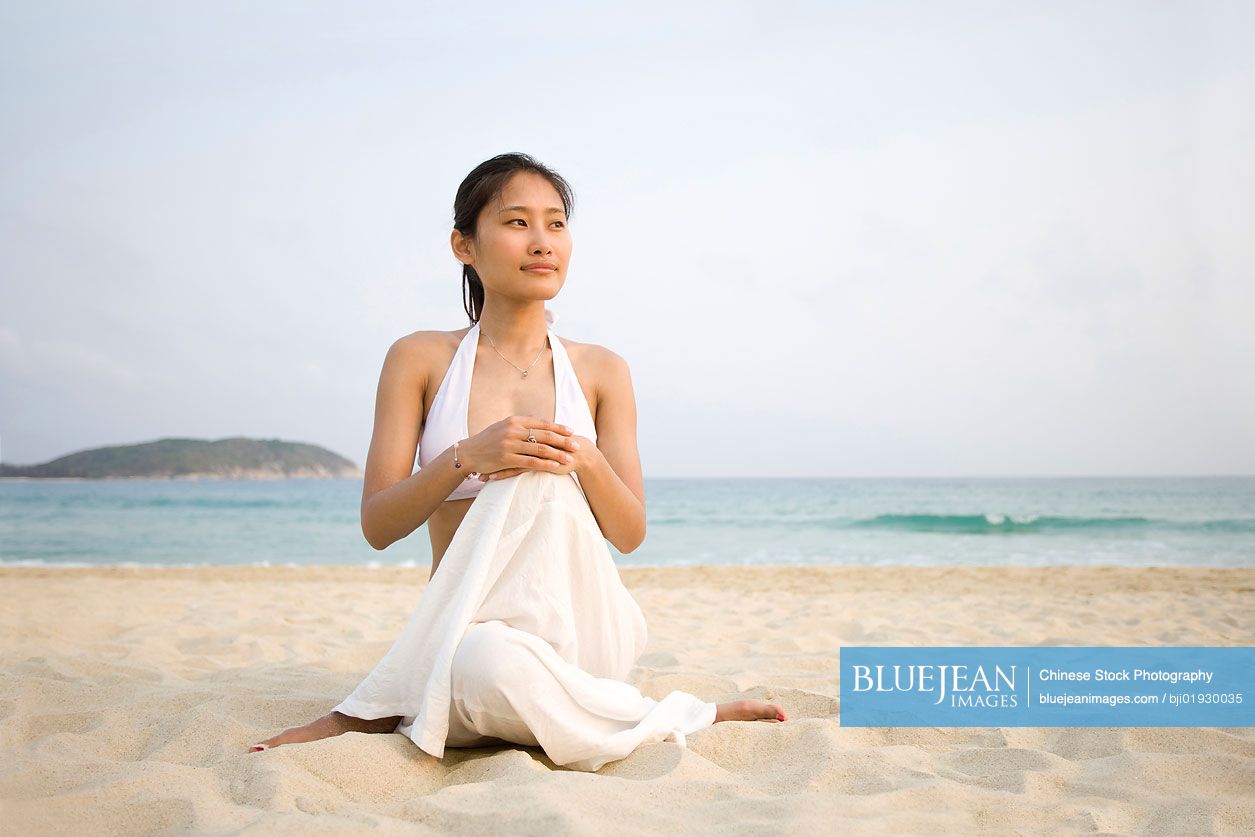 Young Chinese woman doing yoga on the beach