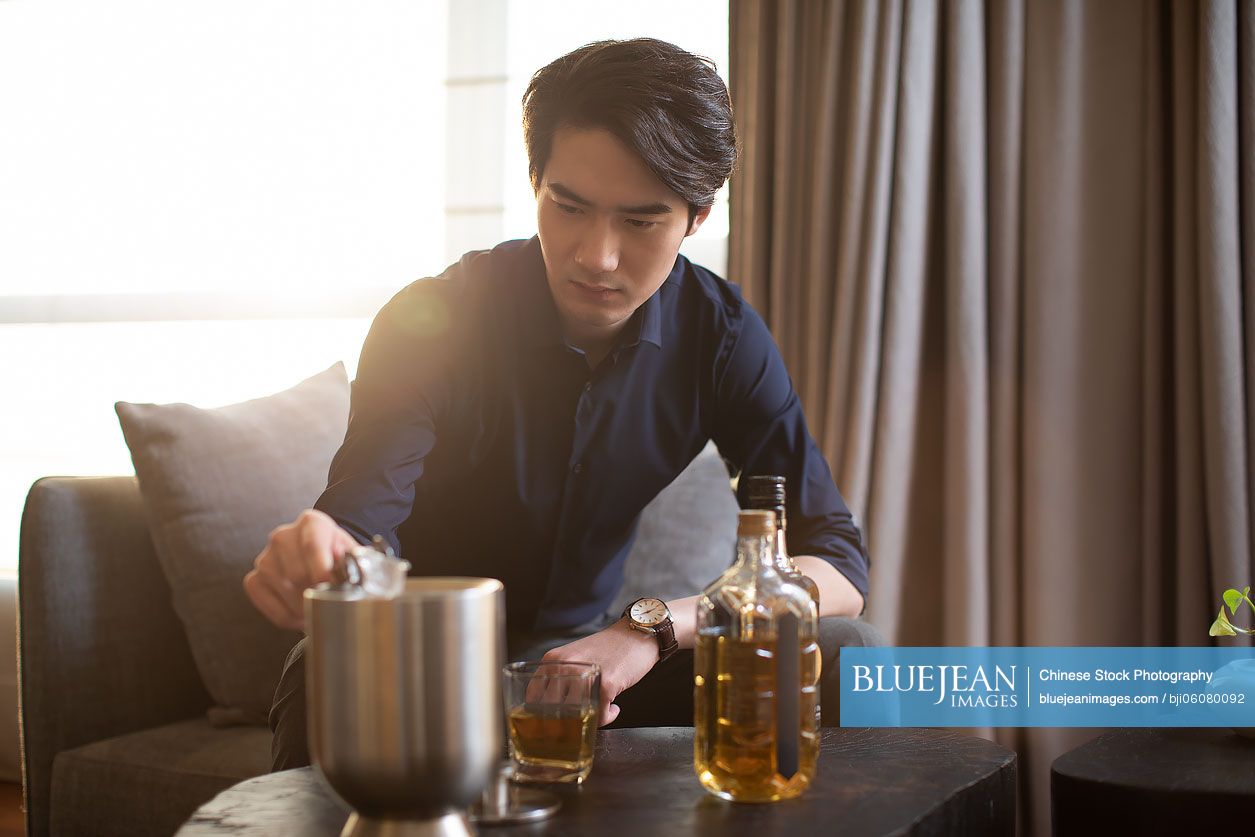 Young Chinese businessman drinking alcohol in hotel room