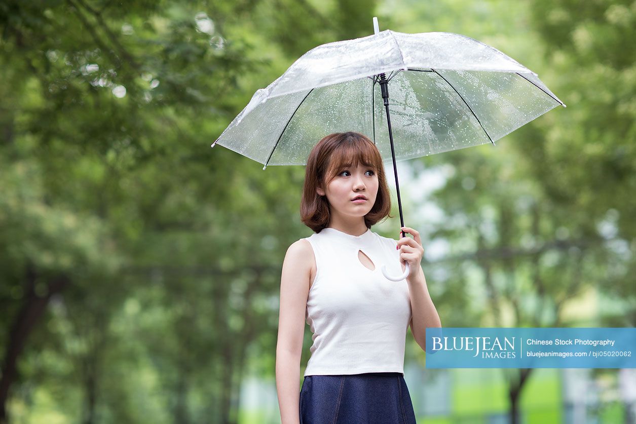Sullen young Chinese woman holding umbrella