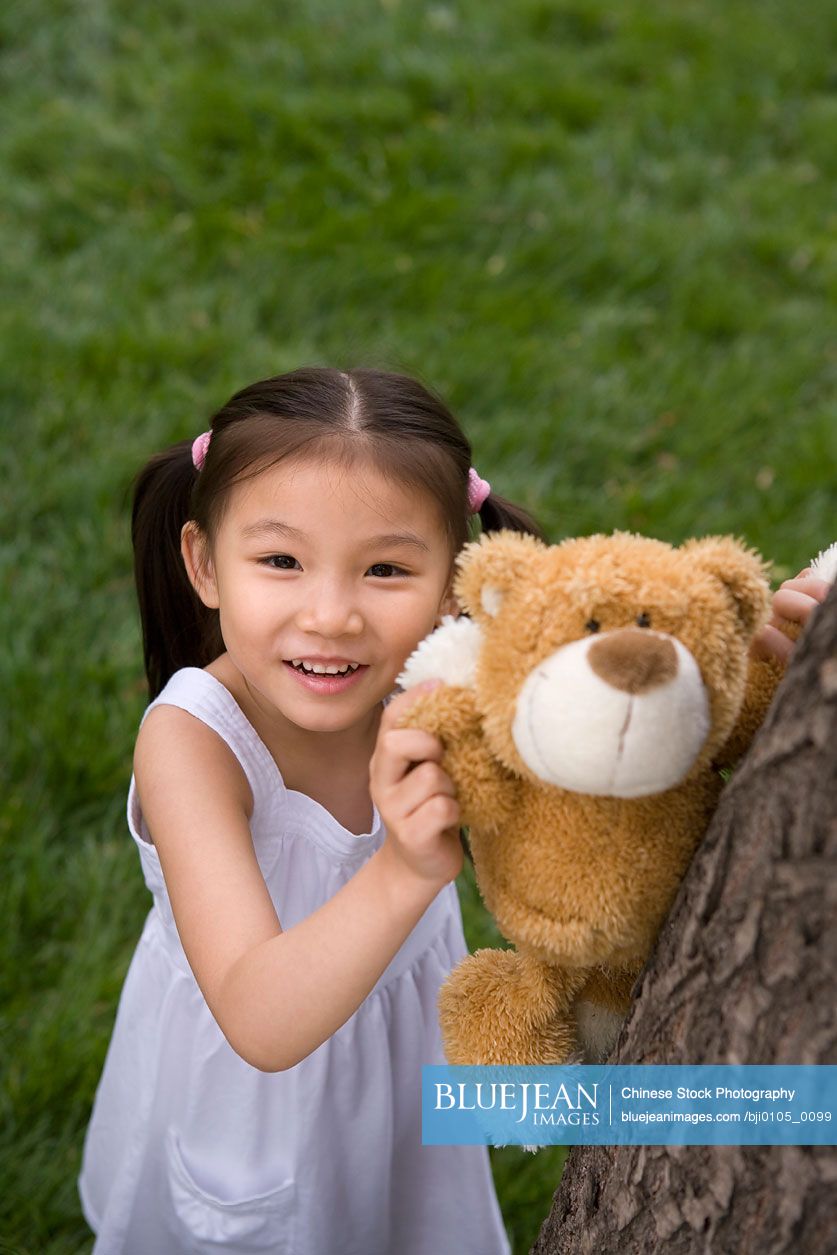 Young Chinese Girl Helping Her Teddy Bear Climb A Tree
