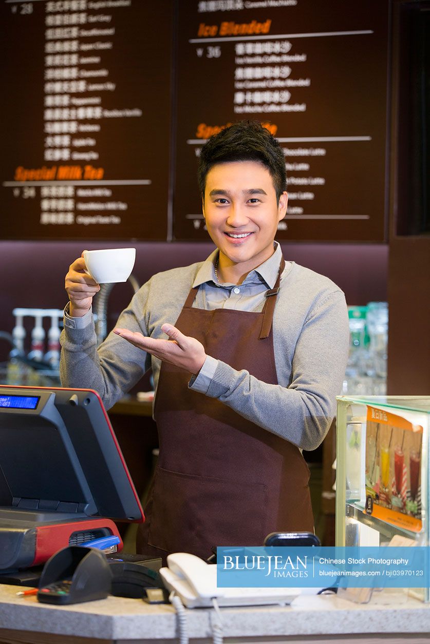 Male Chinese coffee store clerk with cup of coffee in hand